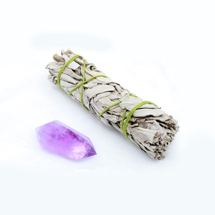 A purple amethyst raw crystal stone with sage to the right of it